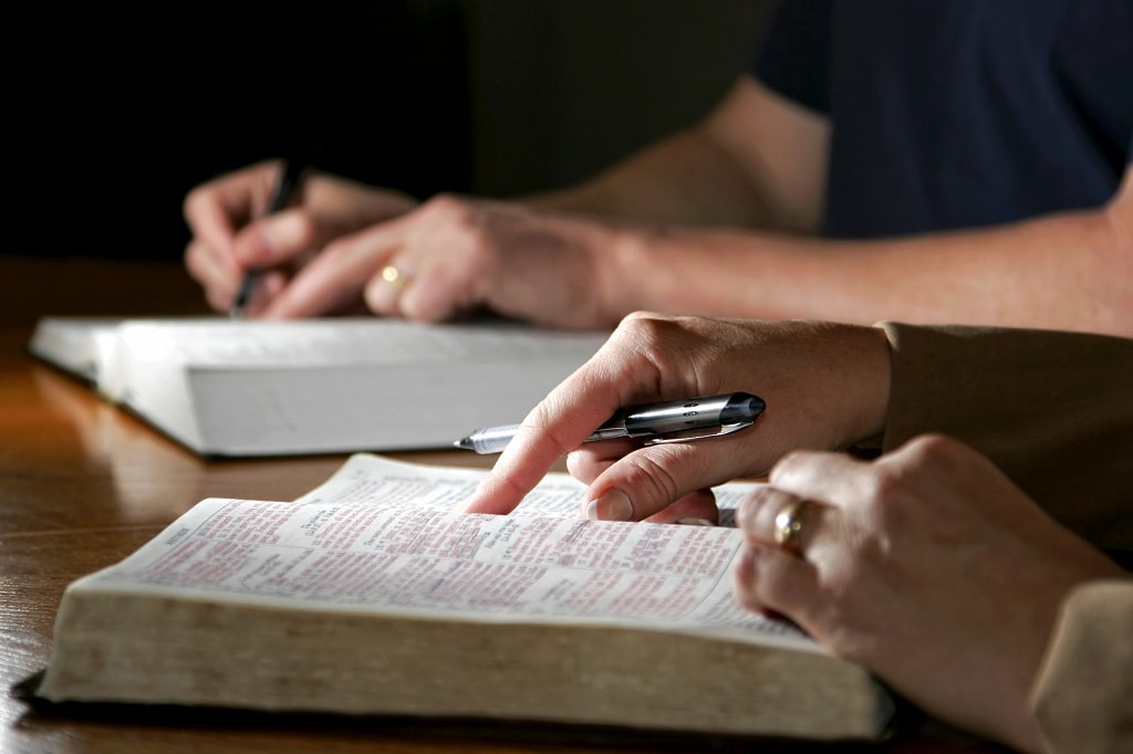 Close up of two people studying the Bible together, taking notes, lectio divina reading